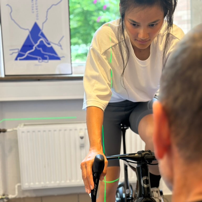 A person receiving a bike fitting session, sitting on a bicycle with the handlebars adjusted to a comfortable height, with a green light pattern indicating areas of adjustment on the bike.