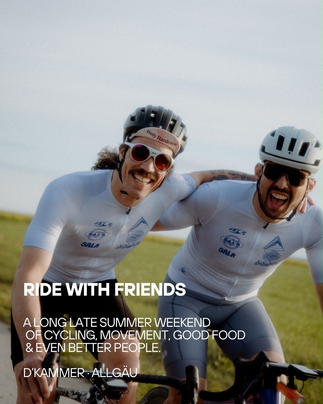Two smiling cyclists outdoors wearing matching white cycling jerseys with blue and black logos, helmets, and sunglasses, with overlaid text reading 'RIDE WITH FRIENDS' and a quote by D'Kammer-Allgäu.