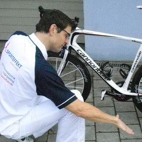 Two people inspecting a white bicycle outdoors.